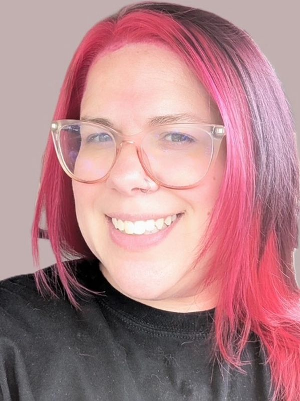 Smiling person with pink and purple hair and glasses.