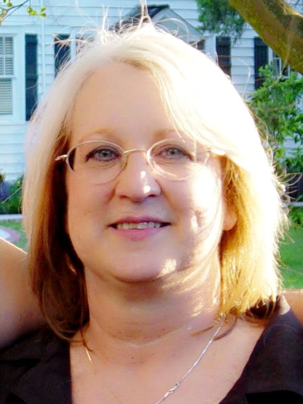Smiling woman with glasses and a cross necklace outdoors.