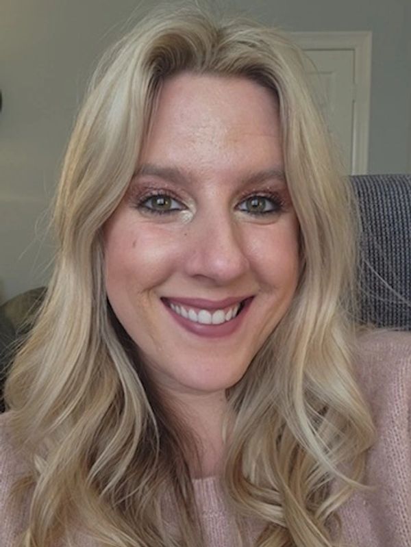 Smiling woman with long blonde hair and light makeup indoors.