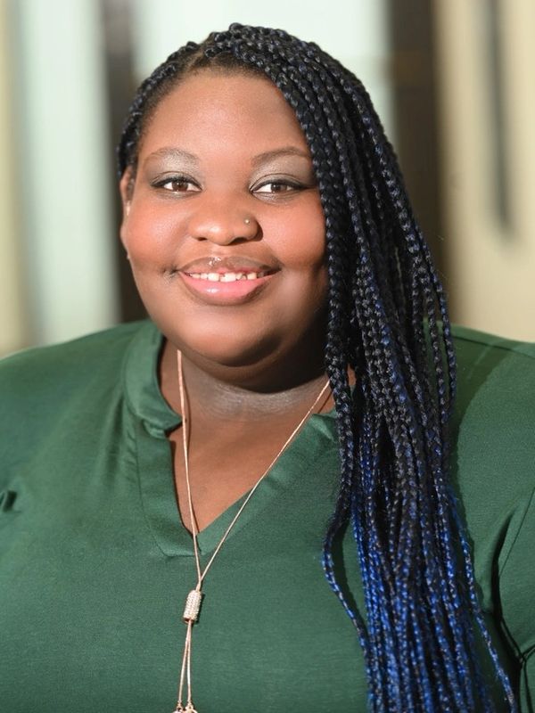 Smiling woman with long braided hair in a green top.