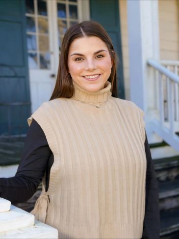 Young woman smiling outdoors in casual beige and black outfit.