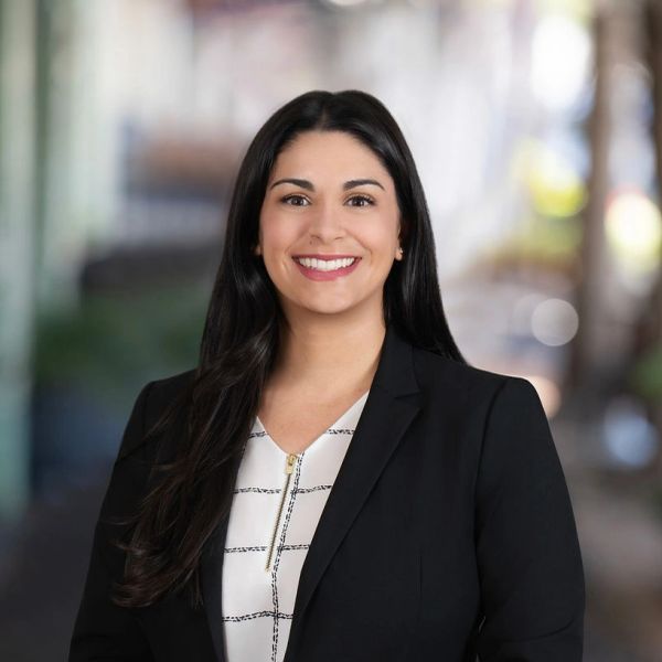 Woman in professional attire smiling outdoors.