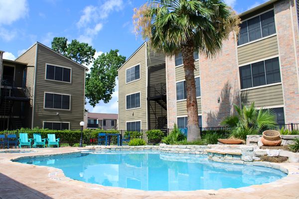 Apartment complex with a swimming pool and palm trees on a sunny day.