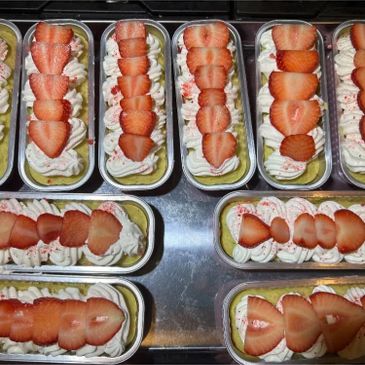 Multiple strawberry-topped desserts in trays.