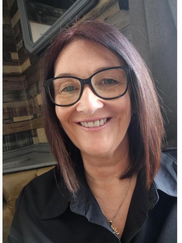 Woman with glasses smiling indoors.