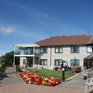 Blue skies, a large two-storey building with a white balcony on the second floor. Stunning gardens.