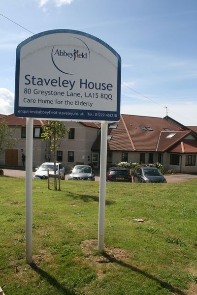 Tall signpost standing in a grassy area. white sign with blue text which says ‘Staveley House, Care 