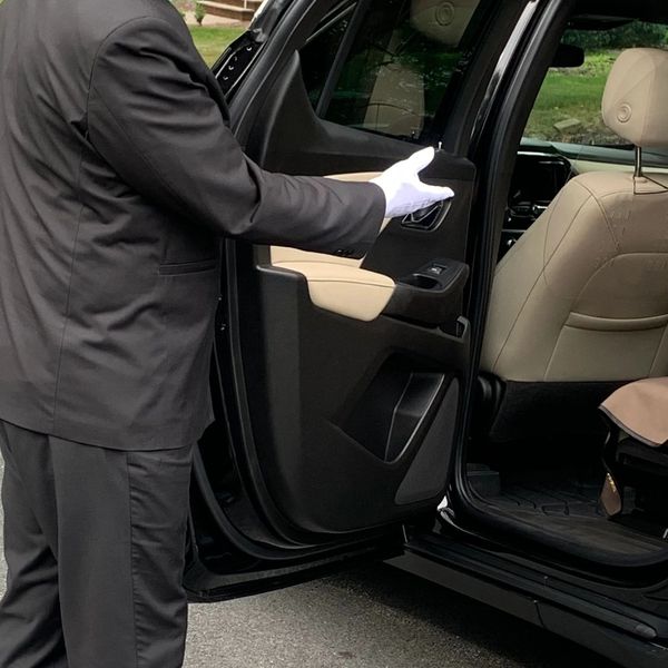 A person in formal gloves opening a car door.