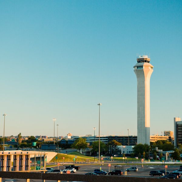 Airport control tower with vehicles and buildings under clear sky.
