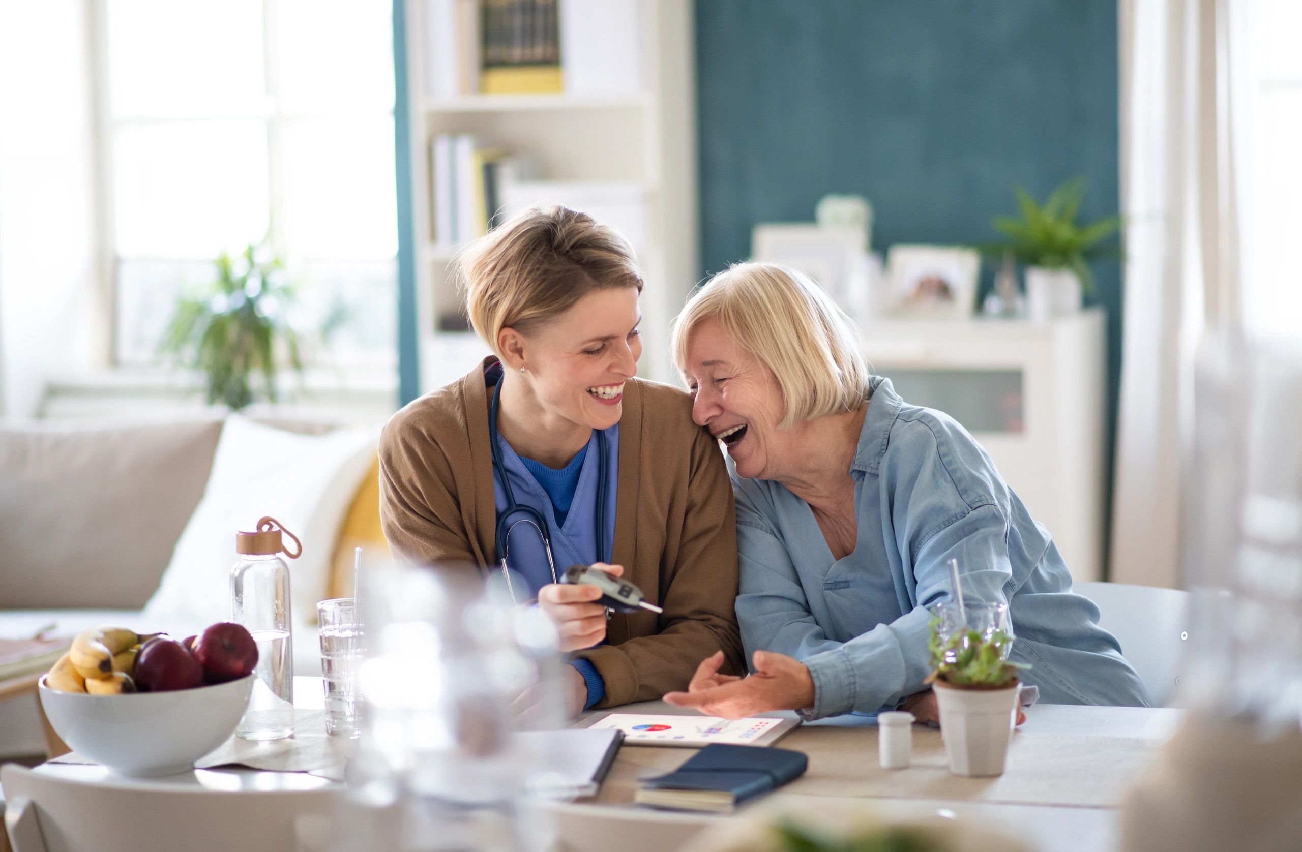 Healthcare worker with laughing senior woman patient, measuring blood glucose indoors