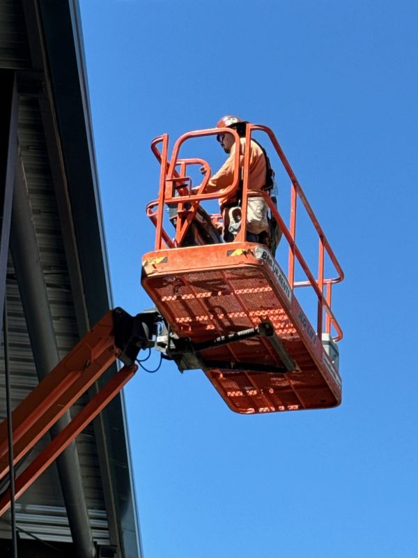 Construction worker using a cherry picker against a clear blue sky.