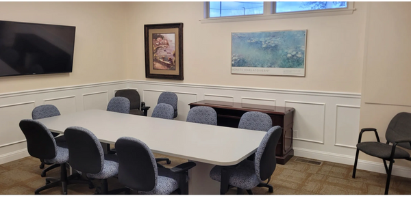 Picture of a board room with a  conference table and chairs, large tv and pictures on the walls