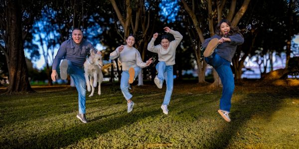 Four people and a dog joyfully jump in a park during the evening.