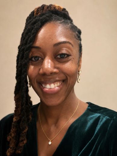 Smiling woman with braided hair and gold jewelry.