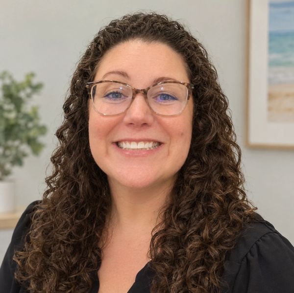 Smiling woman with curly hair and glasses.