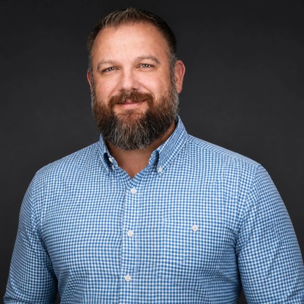 Smiling man with a beard wearing a blue checkered shirt.