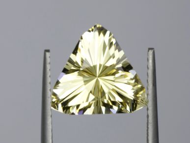 A triangular, pale yellow faceted gemstone held by tweezers.