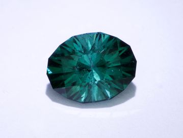 A sparkling green oval-cut gemstone on a white surface.