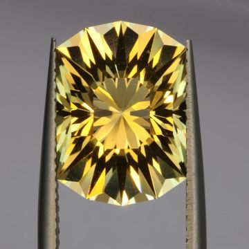 A yellow gemstone held by tweezers with intricate facets.