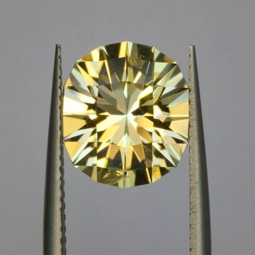 A yellow gemstone held by tweezers against a gray background.