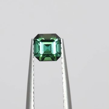 A square-cut green gemstone held by tweezers.