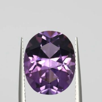 Close-up of a faceted purple gemstone held by tweezers.