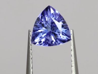 A triangular, faceted blue gemstone held by tweezers.