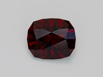 A deep red, faceted gemstone with a cushion cut on a plain background.