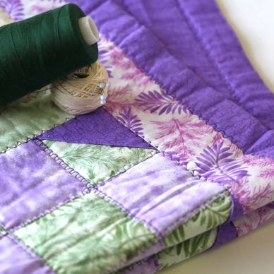 Classic purple and green quilt with spool of quilting thread and pins