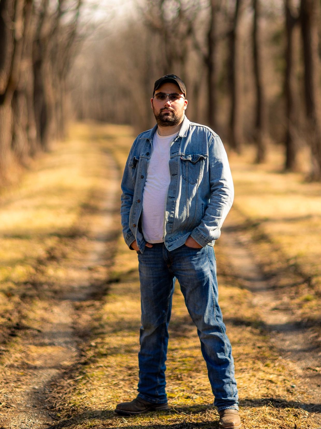 Man in denim jacket and jeans standing on a forest path.