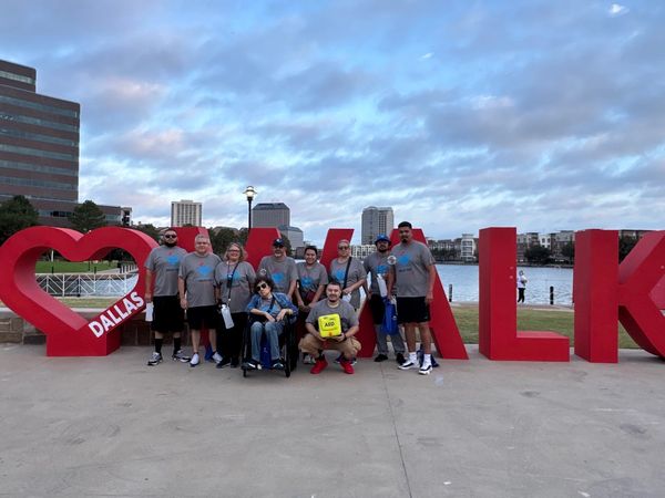 Group photo of people in front of a large red Dallas Walk sign by the water.