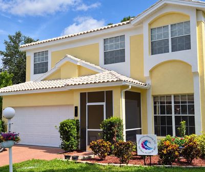 Two-story yellow and white house with a garden.