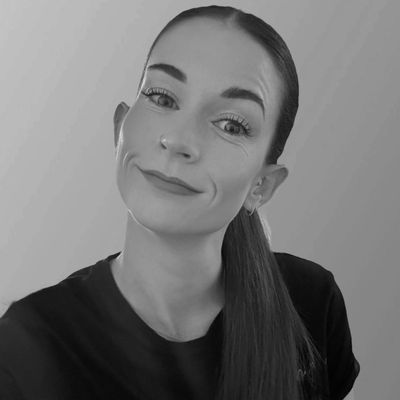 A woman with red hair tied back, wearing a black shirt, smiles against a purple background.
