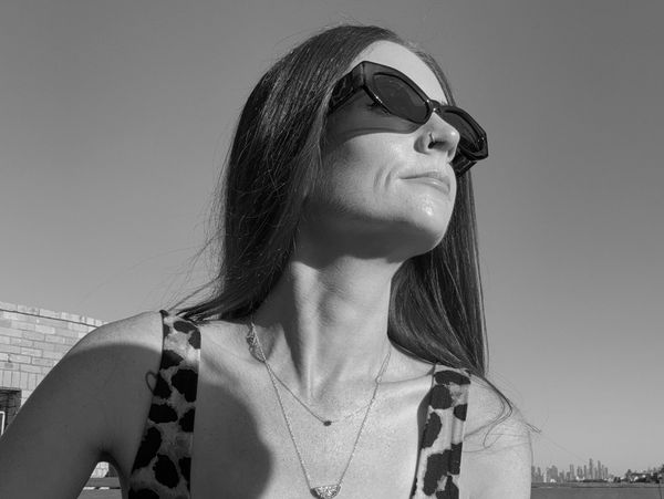 Woman with red hair wearing sunglasses and leopard print top holding a blue coffee cup.