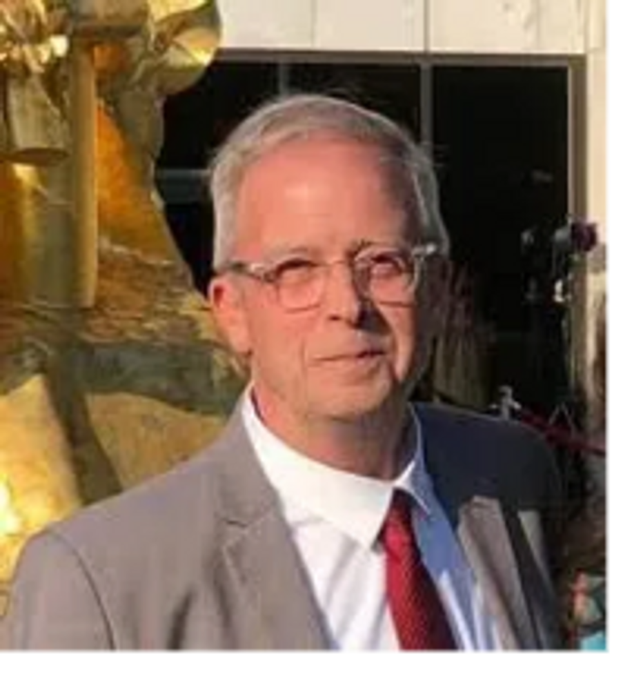 A man in a suit and red tie standing outdoors in sunlight.