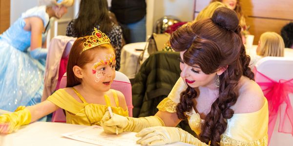 A little girl in a princess dress and face paint talks to a woman dressed as Belle from Beauty and the Beast.