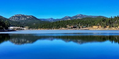 Clear blue lake reflecting forested mountains under bright sky.