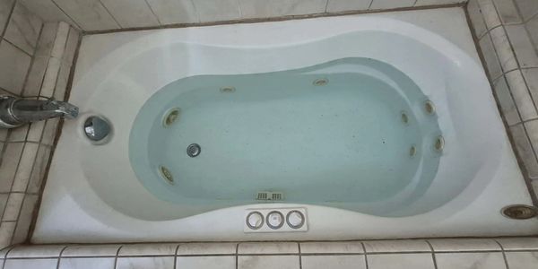 Jacuzzi Jetted bathtub with tile surrounding and water filled to cover jets showing 3 button topside