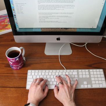 Person typing on a keyboard with a coffee mug nearby on a wooden desk.