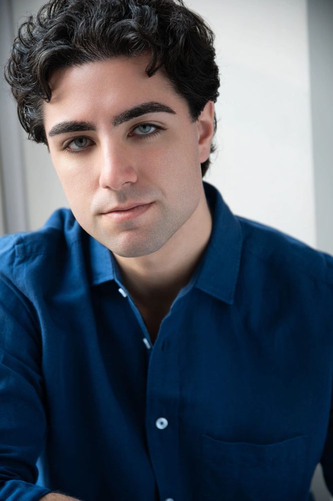 Portrait of a young man with curly hair wearing a blue shirt.