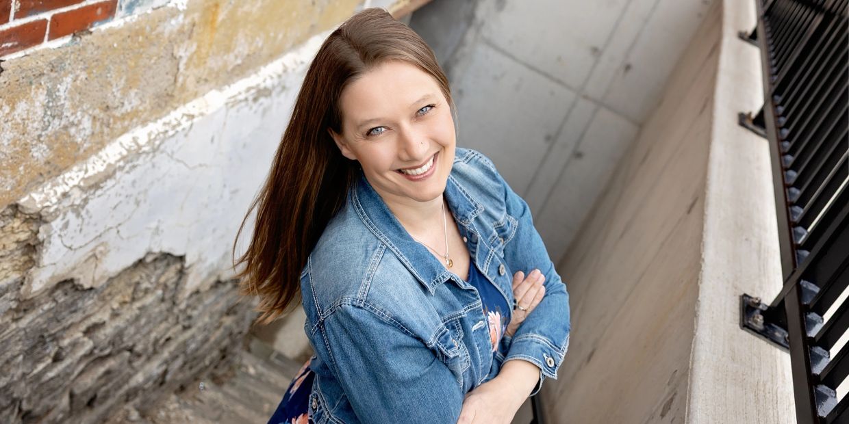 Woman smiling in denim jacket on stairs.