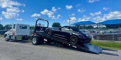 Low clearance luxury AWD car loading on flatbed tow truck using ramps