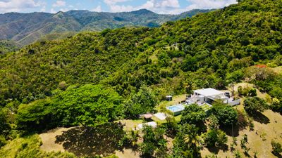 A house surrounded by lush green hills and trees under a blue sky.
