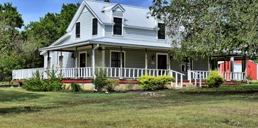 A classic white farmhouse with a wraparound porch and a red barn in the background.