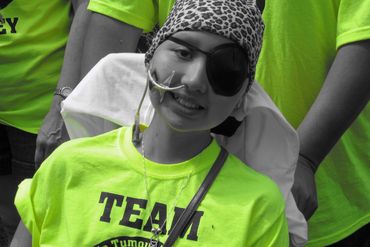 Young girl with an eyepatch and nasal tube wearing a bright green team shirt.