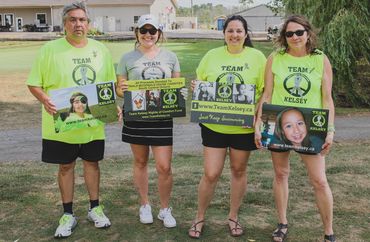 Four individuals wearing neon green shirts hold signs supporting Team Kelsey outdoors.