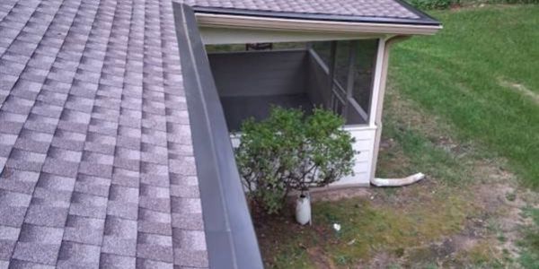 View of a rooftop with a gutter and a small tree near a screened porch.