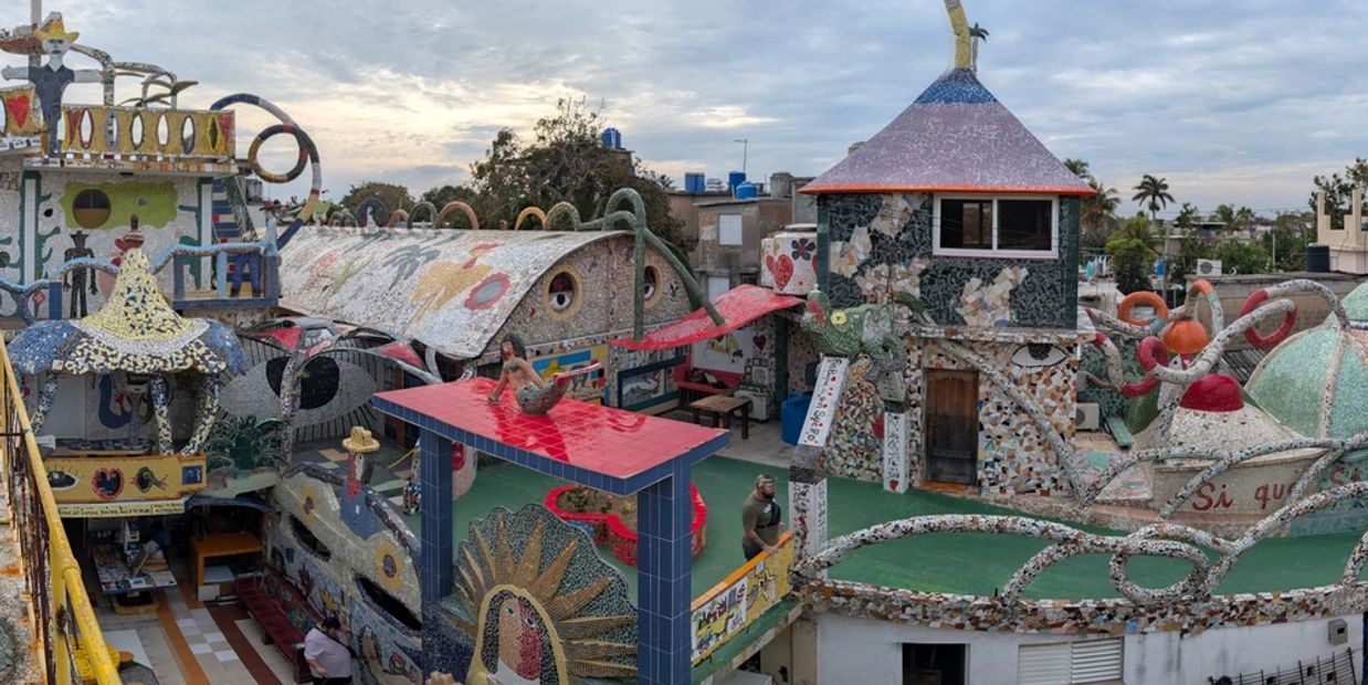 Colorful mosaic-covered buildings and sculptures with a cloudy sky.