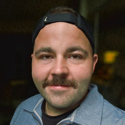Close-up of a man with a mustache and backward cap smiling.