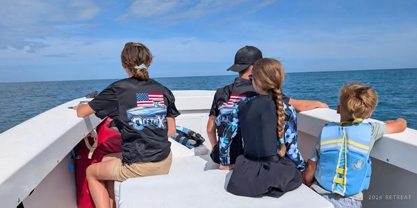 An OTX family sits together on a boat, photographed from behind to protect their privacy.